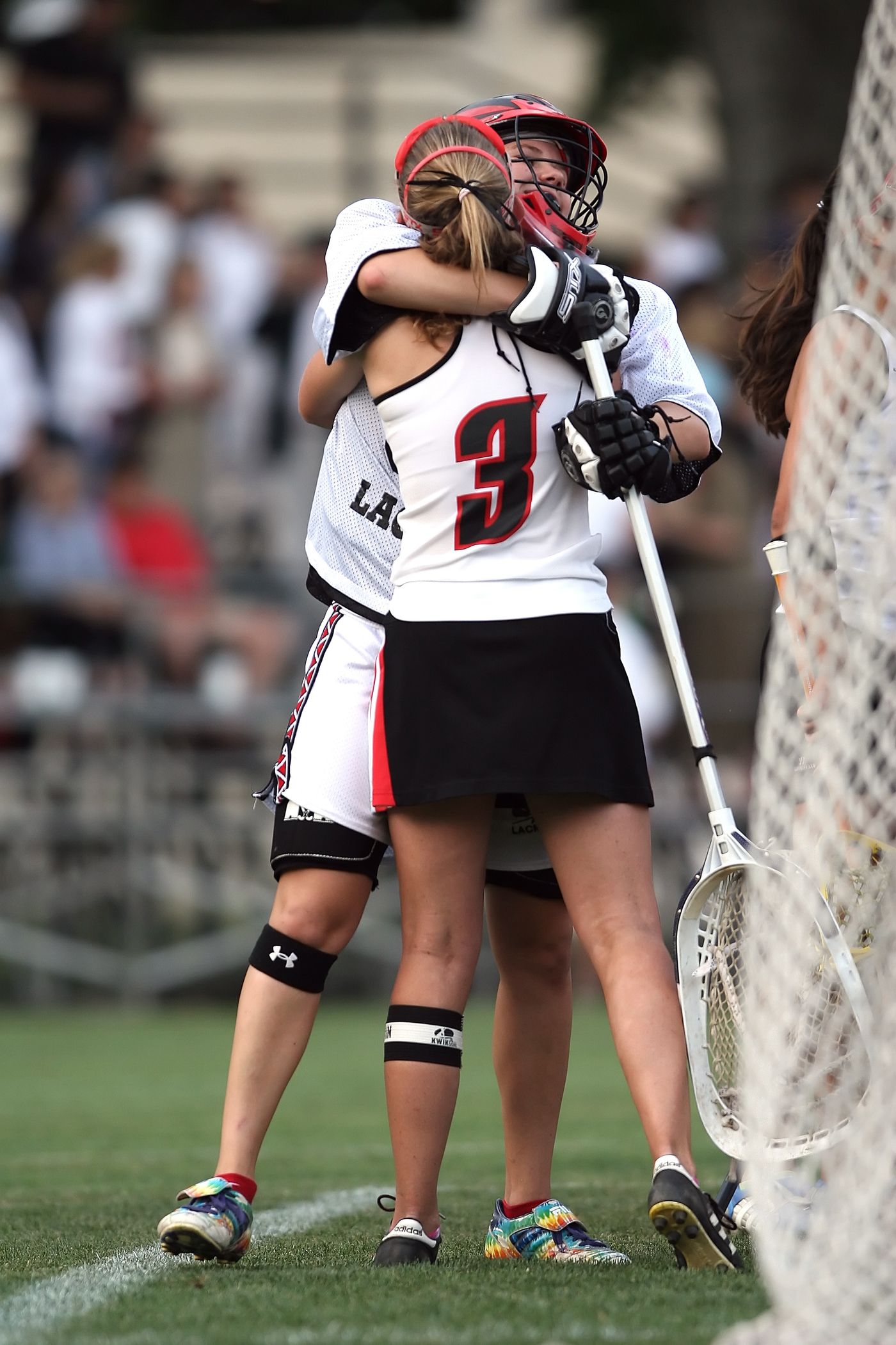 Two girls' lacrosse teammates embracing on the field to celebrate after a goal.