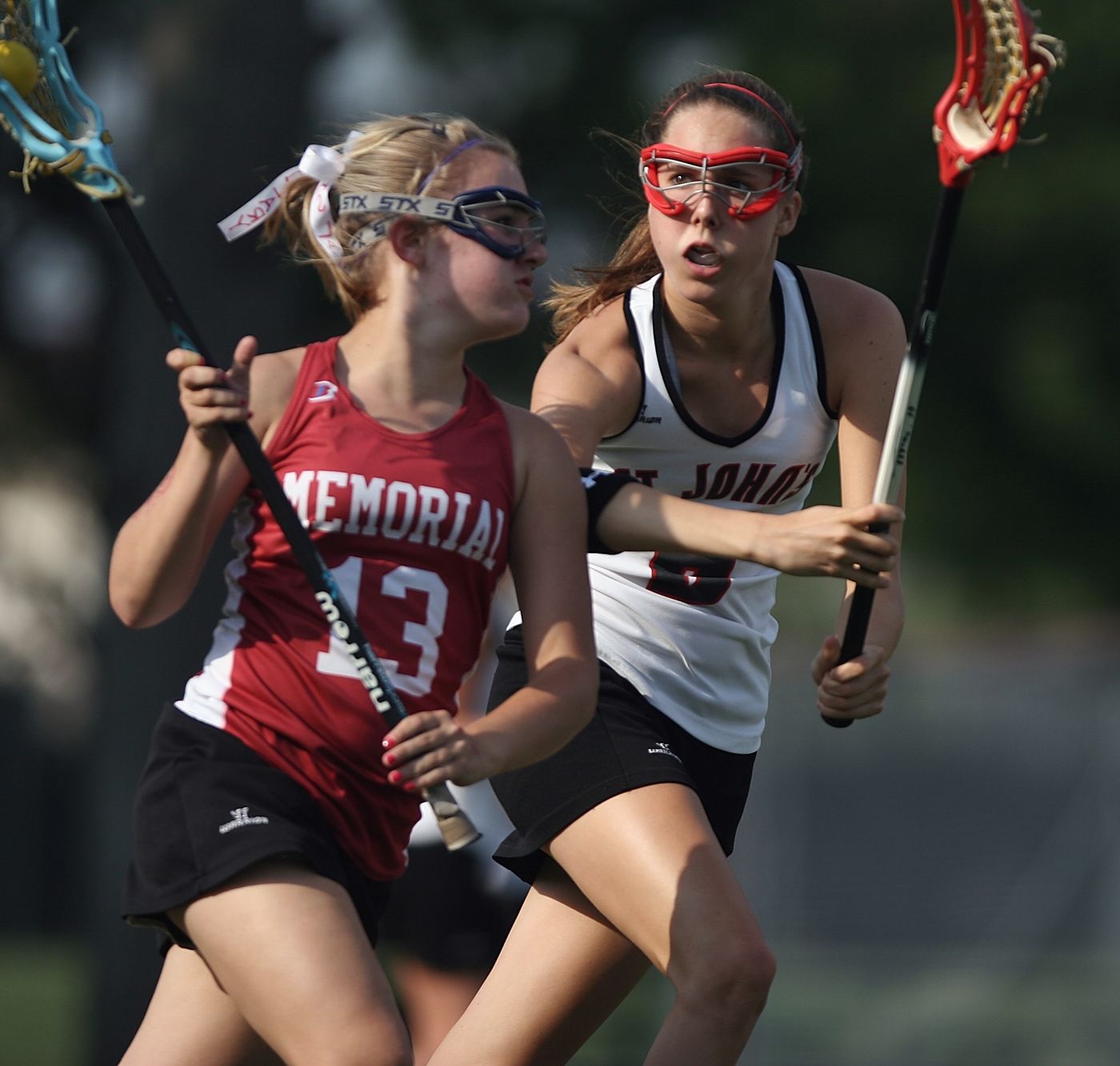 Two high school girls' lacrosse players in goggles running stride for stride during a game.