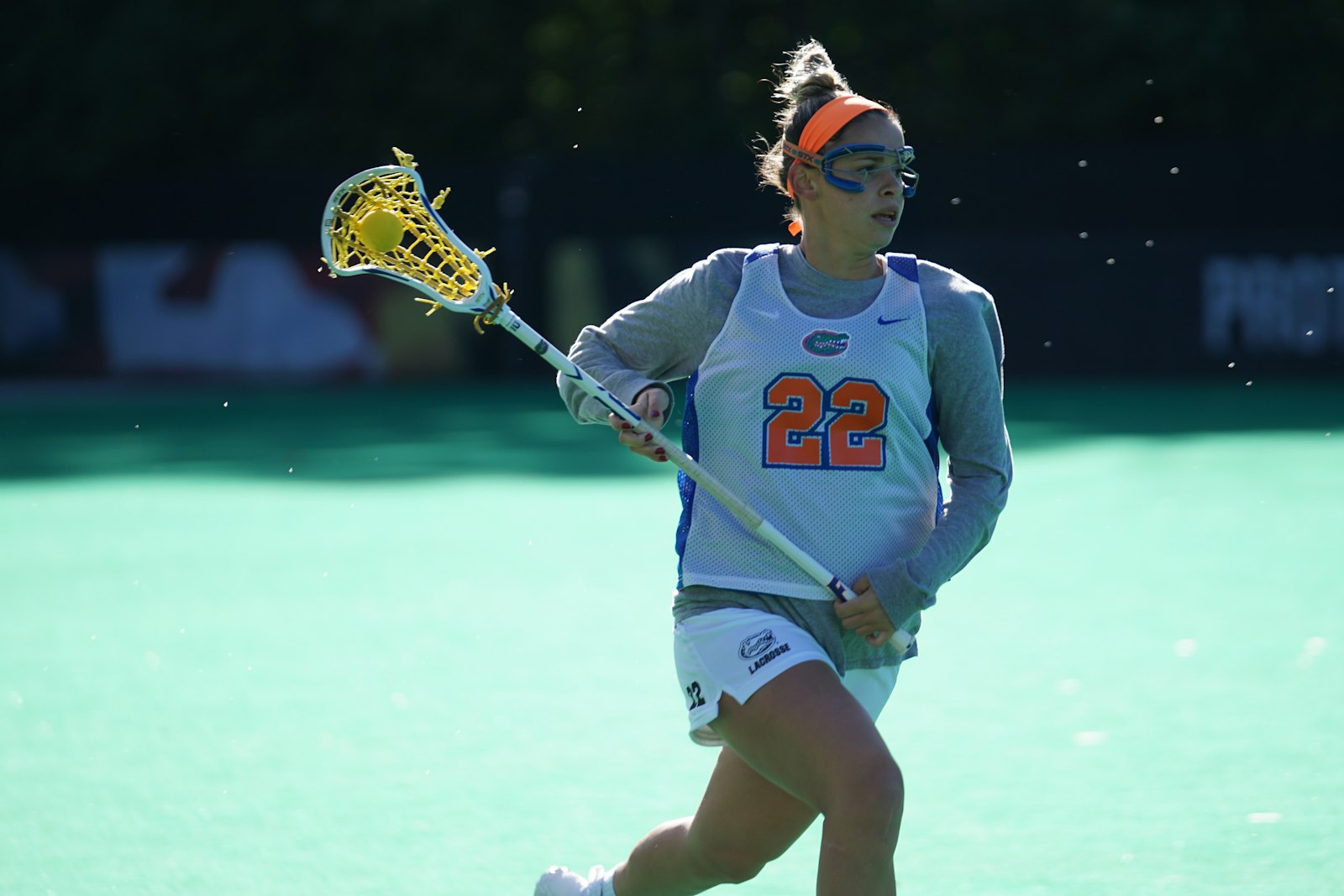 A women's lacrosse player carrying the ball in her stick as she drives upfield.